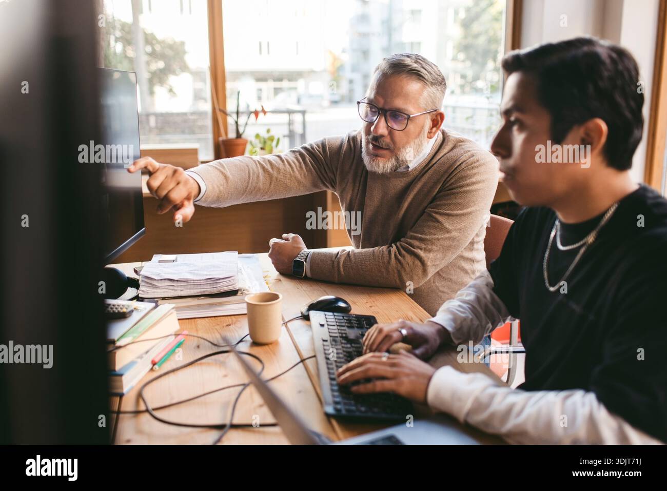 Uomo d'affari maturo che assiste un collega maschio che lavora al computer in un'azienda di progettazione Foto Stock