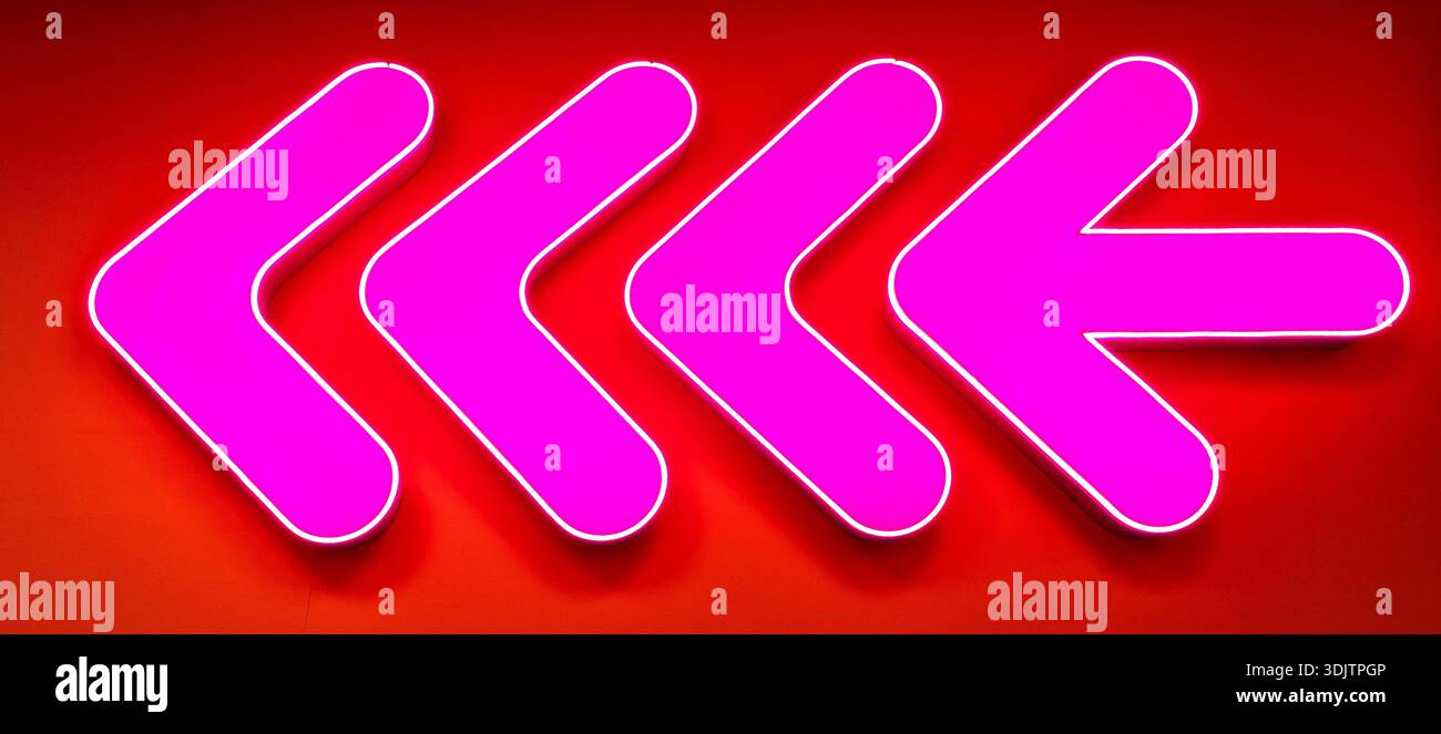 Freccia al neon rosa brillante. Puntatore a freccia al neon luminoso sulla parete di un edificio. Cartello con tubi al neon luminosi Foto Stock