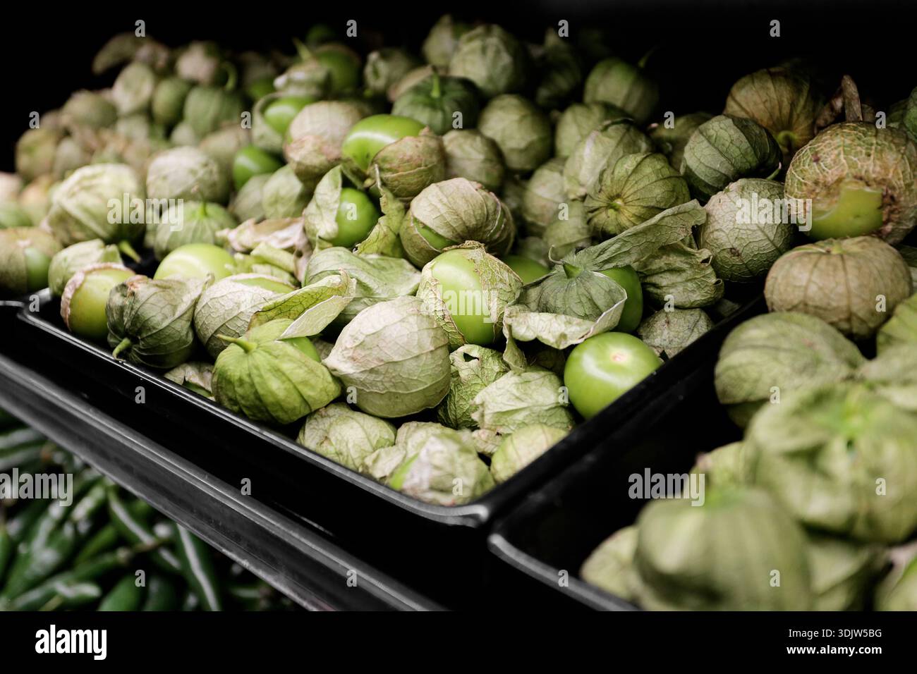 Tomatillo verde fresco esposto nella cassa del mercato. Verdure crude con bucce pronte per la cottura. Ingredienti alimentari sani e prodotti alimentari di base Foto Stock