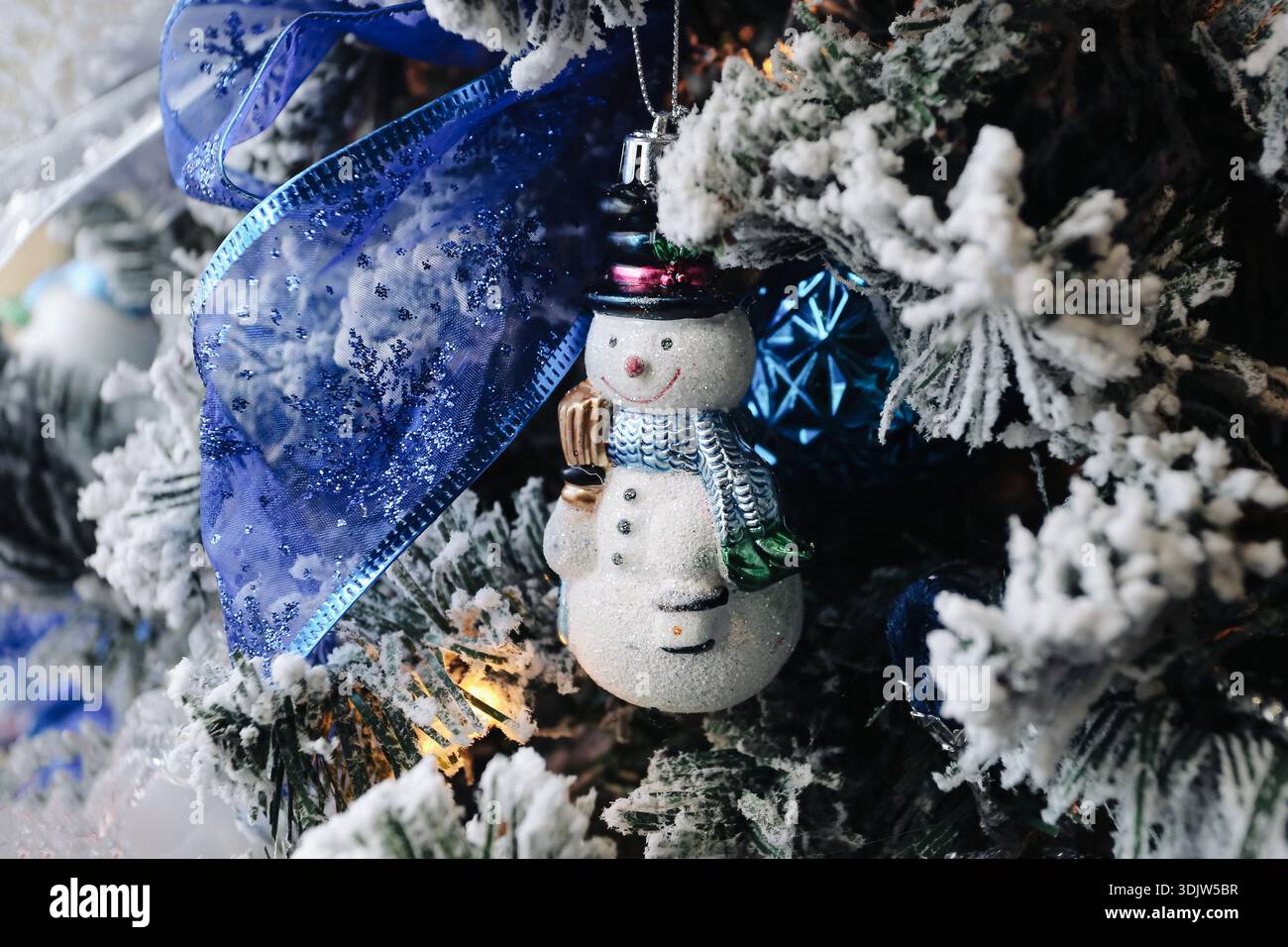 Decorazione dell'albero di Natale con ornamento di pupazzo di neve tra rami smerigliati e nastro blu. Decorazioni per le vacanze invernali con un'atmosfera festosa. Foto Stock