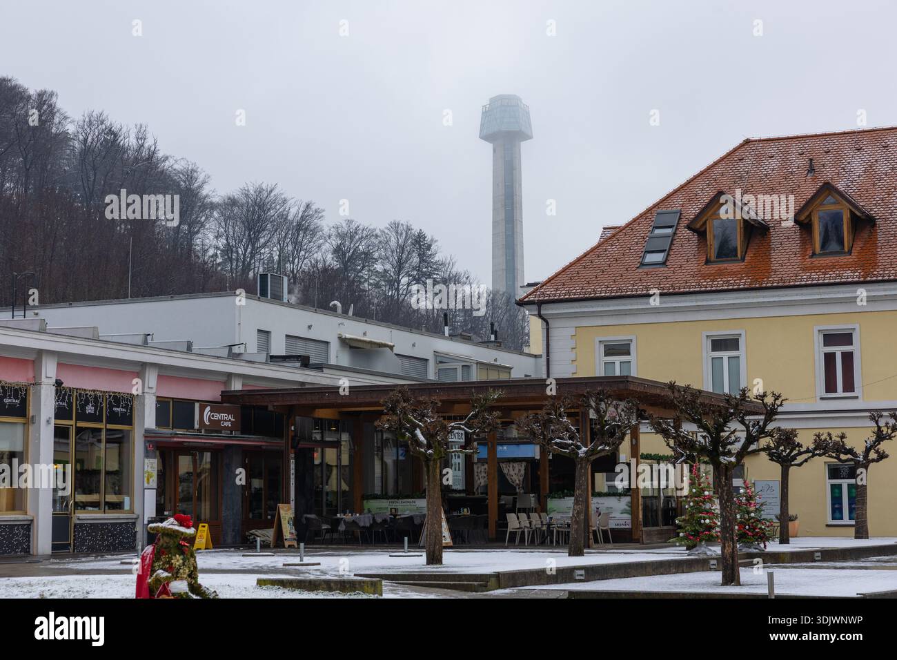 ROGASKA SLATINA, SLOVENIA, 01.03.2026: Scena della piazza della città spolverata di neve con un caffè, posti a sedere all'aperto, alberi potati, un allegro albero di Natale e un Foto Stock