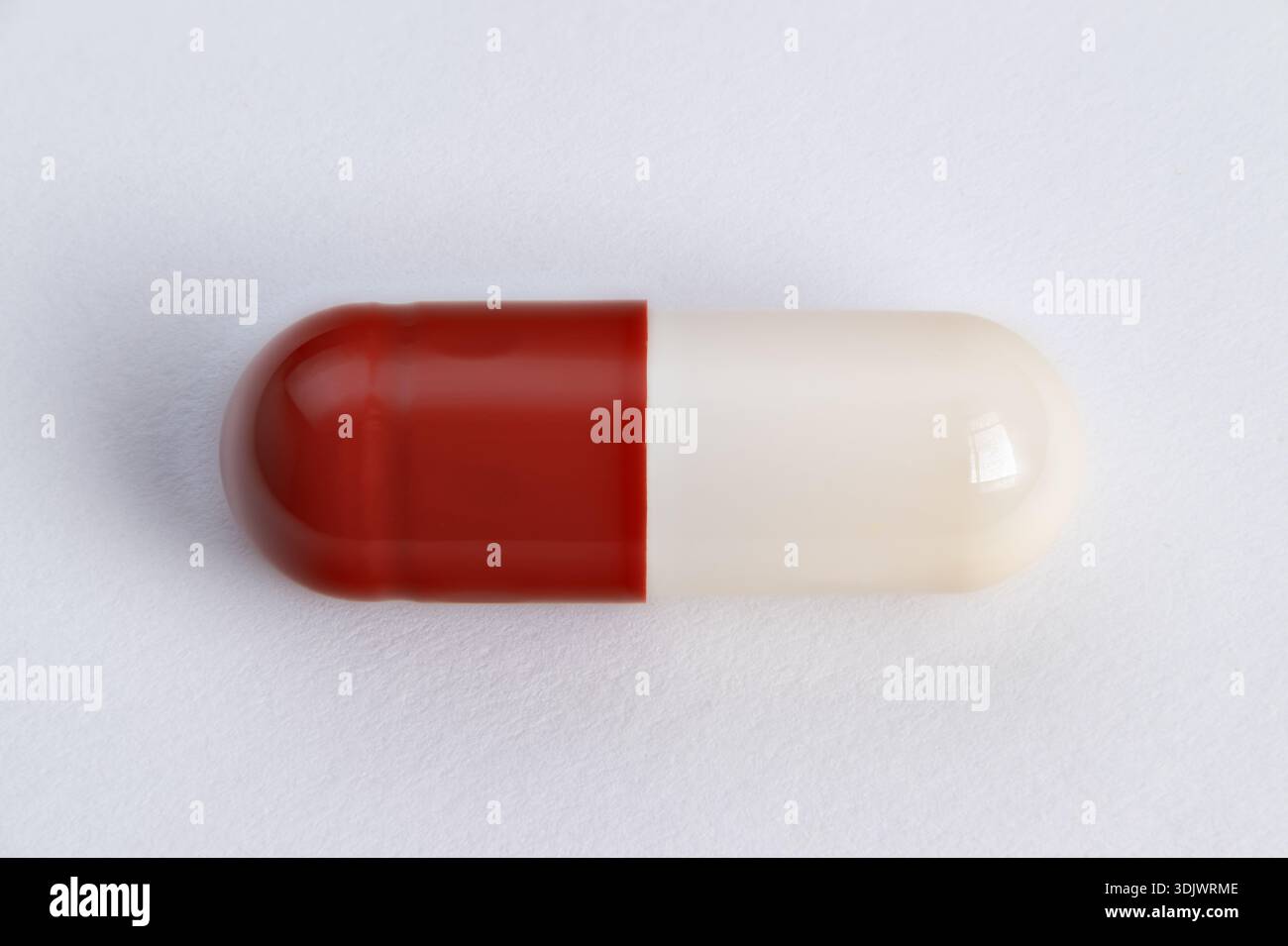 primo piano di una capsula singola rossa e bianca che mette in risalto la superficie lucida e la cucitura, foto di un prodotto macro per il branding e il confezionamento, isolata su un backgrou neutro Foto Stock