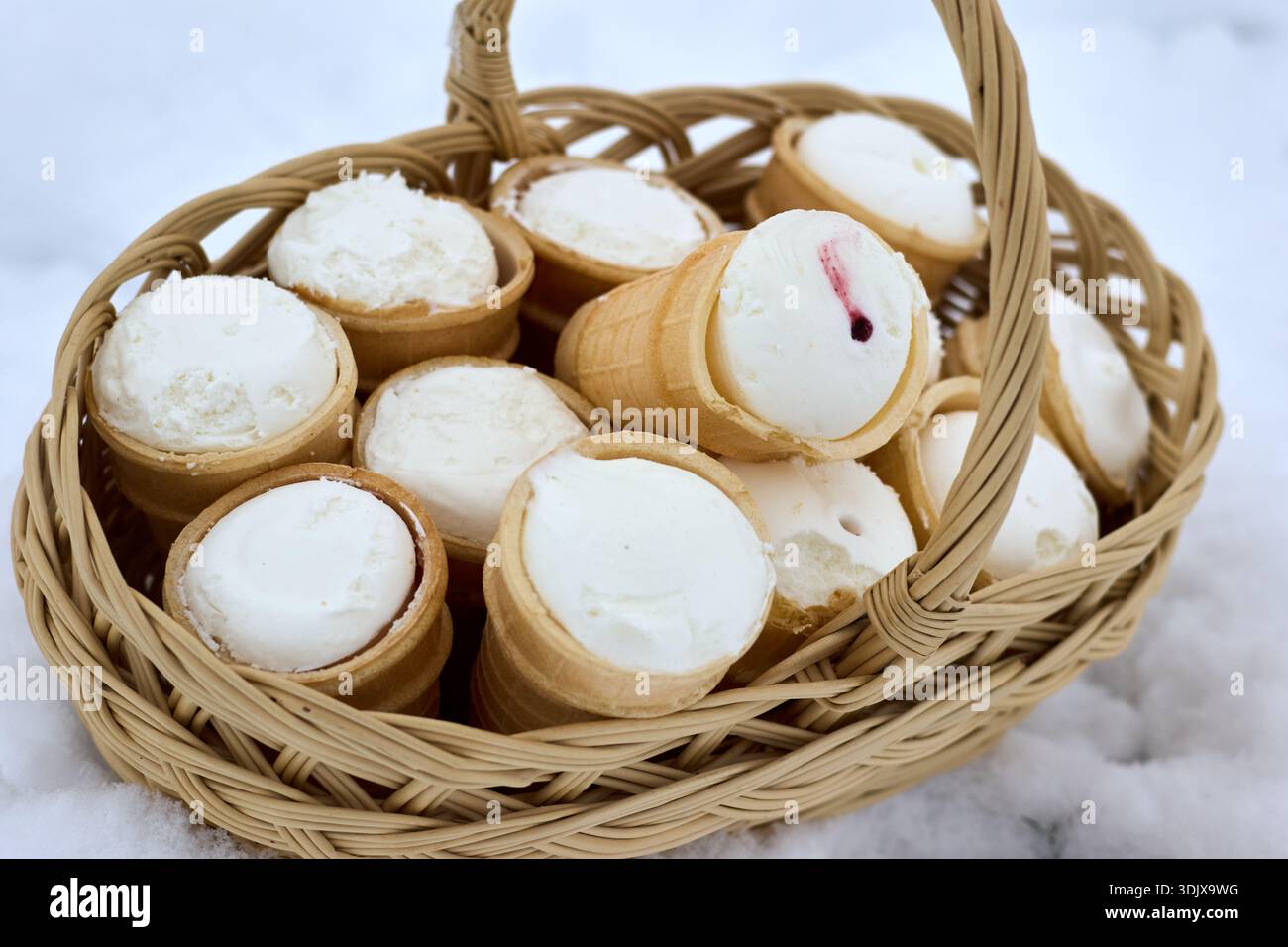 Questa immagine mostra un affascinante cestino di vimini pieno di tazze per waffle riempite di cremoso gelato bianco alla vaniglia. La scena è ambientata all'aperto, con Foto Stock
