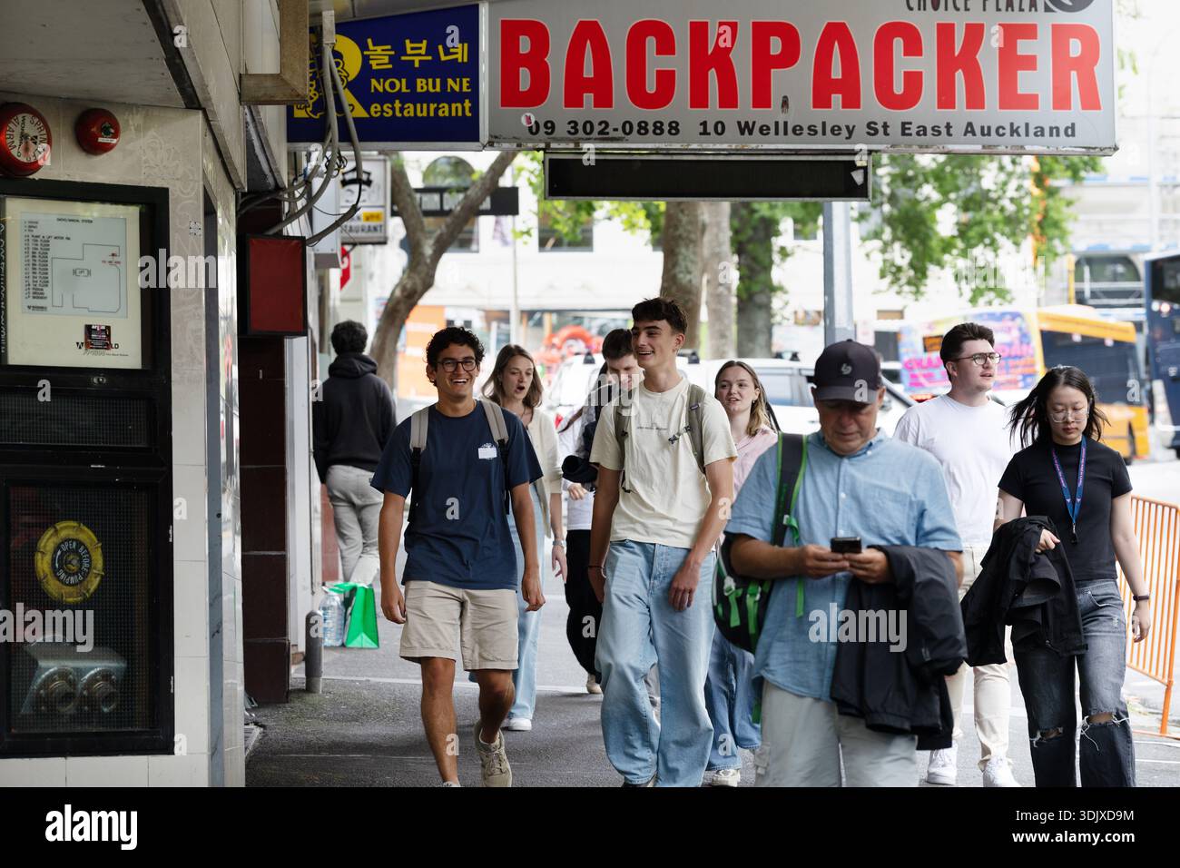 I pedoni camminano lungo Queen Street sotto un cartello per backpacker Hostel nel centro di Auckland, nuova Zelanda. Foto Stock