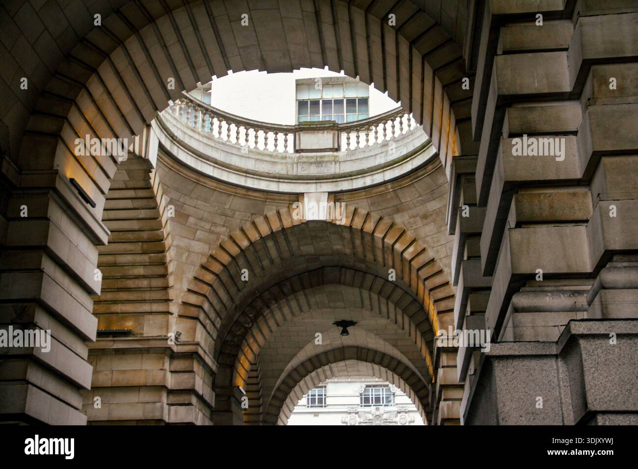 Vista ad angolo basso di archi concentrici in pietra e balaustra decorativa in un edificio classico, che mostra simmetria architettonica neoclassica. Foto Stock