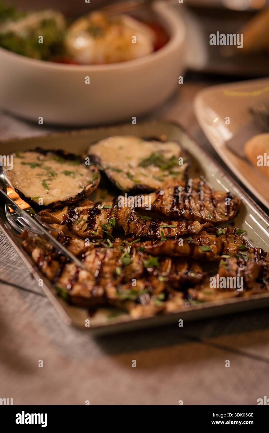 Verdure miste grigliate condite con formaggio fuso ed erbe fresche, servite su un piatto rustico in una presentazione gastronomica in stile ristorante Foto Stock