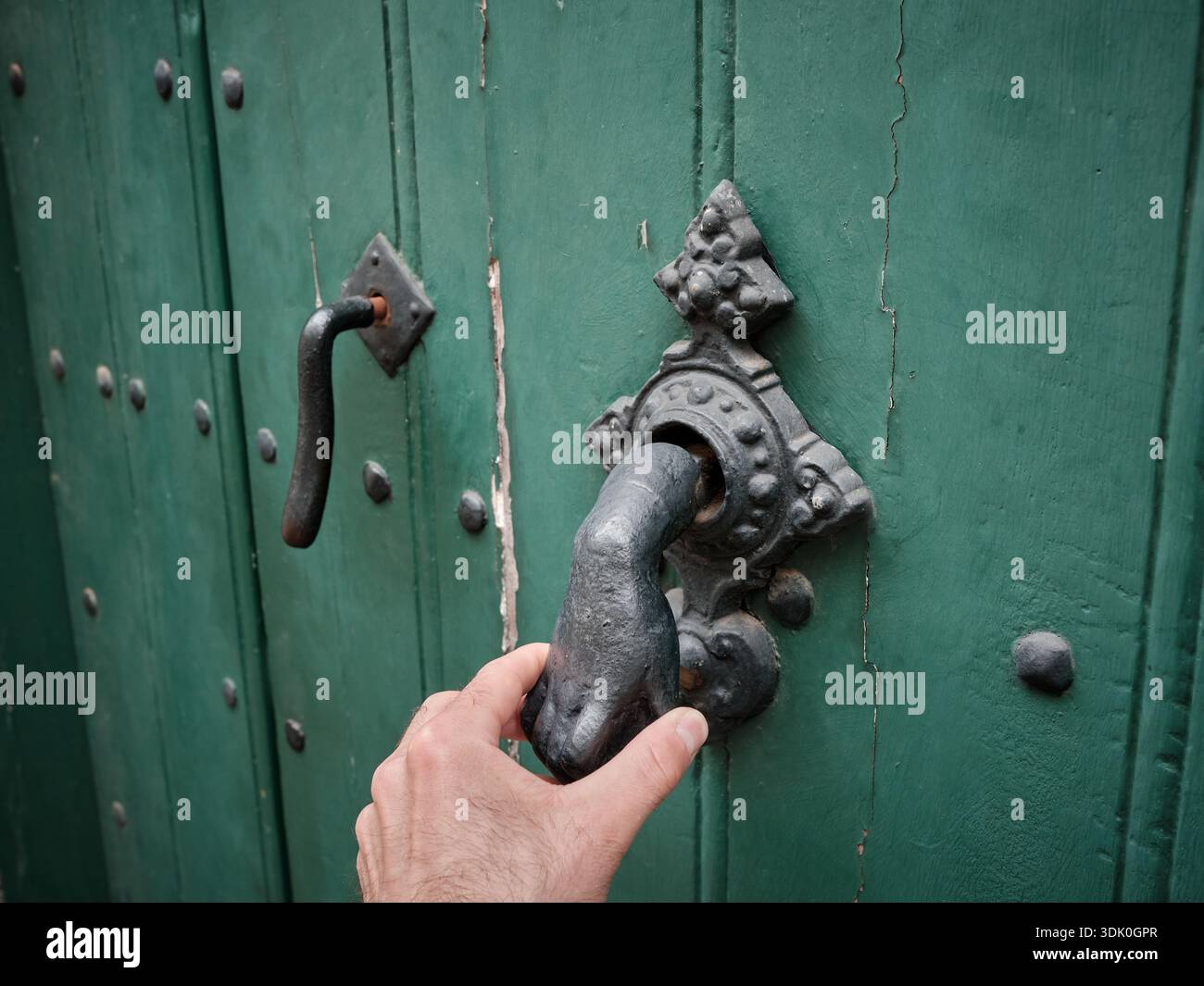 Afferrare a mano una maniglia in metallo ornata su una vecchia porta di legno verde, che simboleggia l'accesso, l'ingresso e il benvenuto. Foto Stock