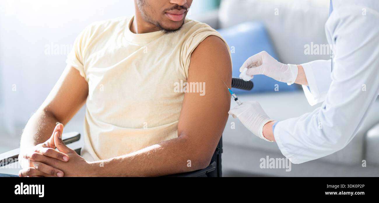 L'uomo con pelle scura riceve una vaccinazione mentre usa una sedia a rotelle in una stanza luminosa Foto Stock