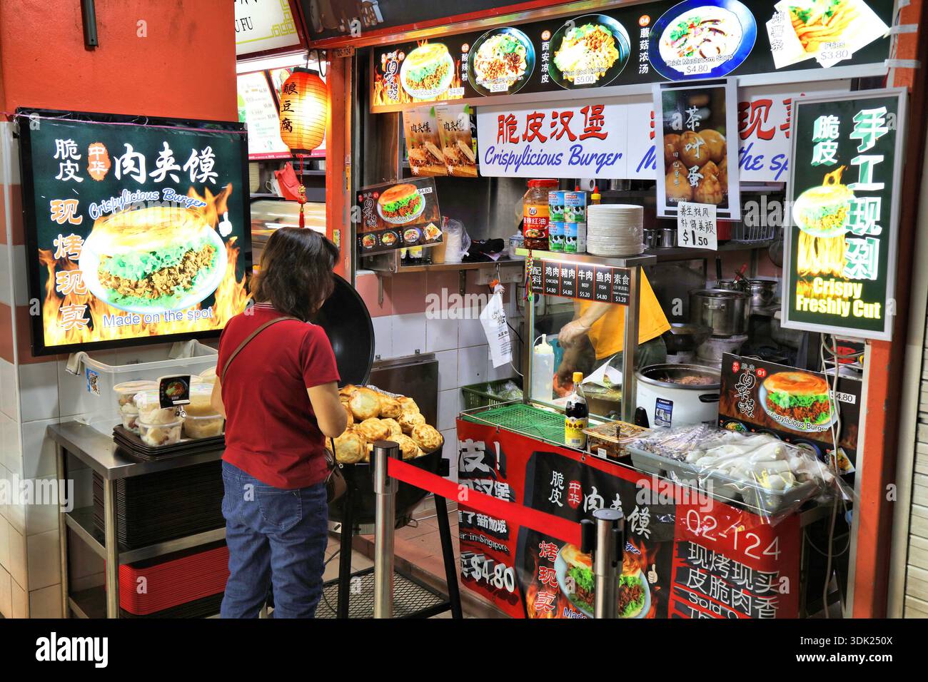 CITTÀ DI SINGAPORE, SINGAPORE - 13 MARZO 2024: Le persone visitano il ristorante Crispylicious Burger al Chinatown Complex, l'area ristoro del centro hawker di Singapore. Foto Stock