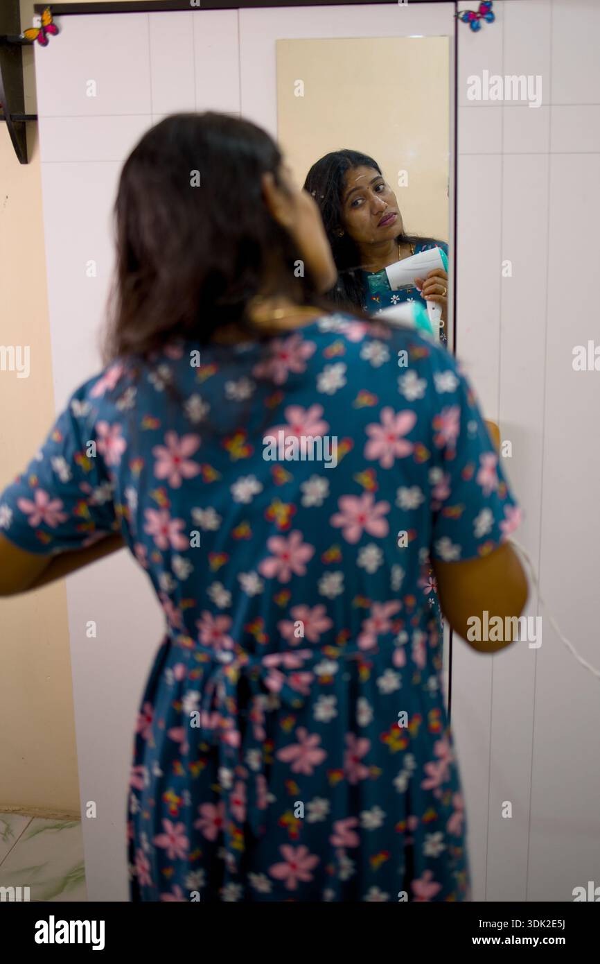 Una donna sta di fronte a uno specchio, preparandosi ad un evento. Foto Stock