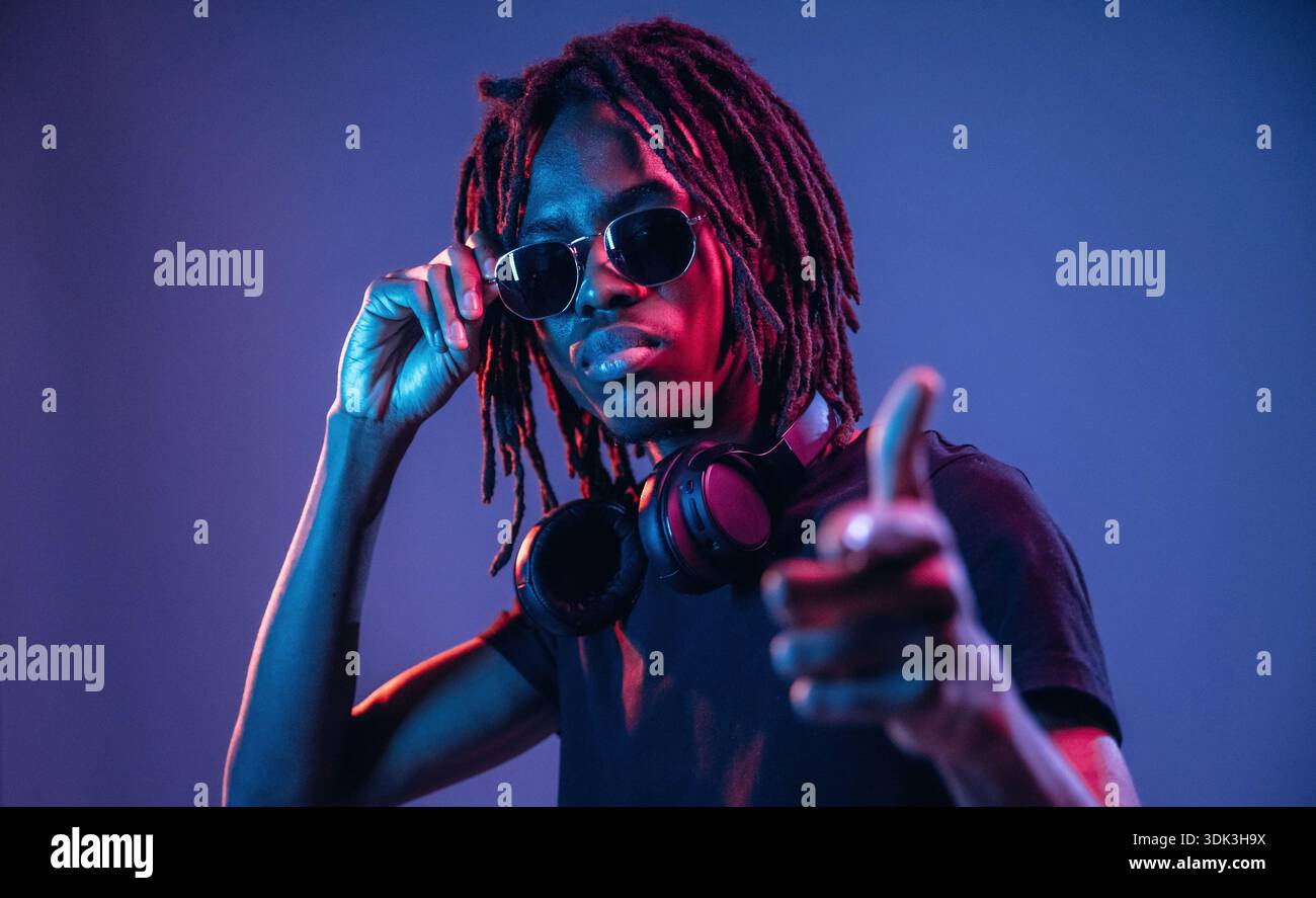 Puntando con il dito, con gli occhiali da sole. L'afroamericano è uno studio con illuminazione al neon. Foto Stock