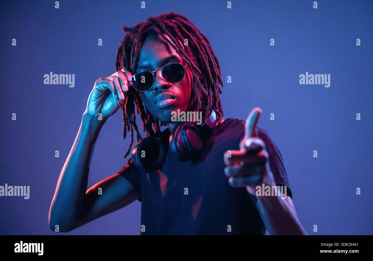 Puntando con il dito, con gli occhiali da sole. L'afroamericano è uno studio con illuminazione al neon. Foto Stock