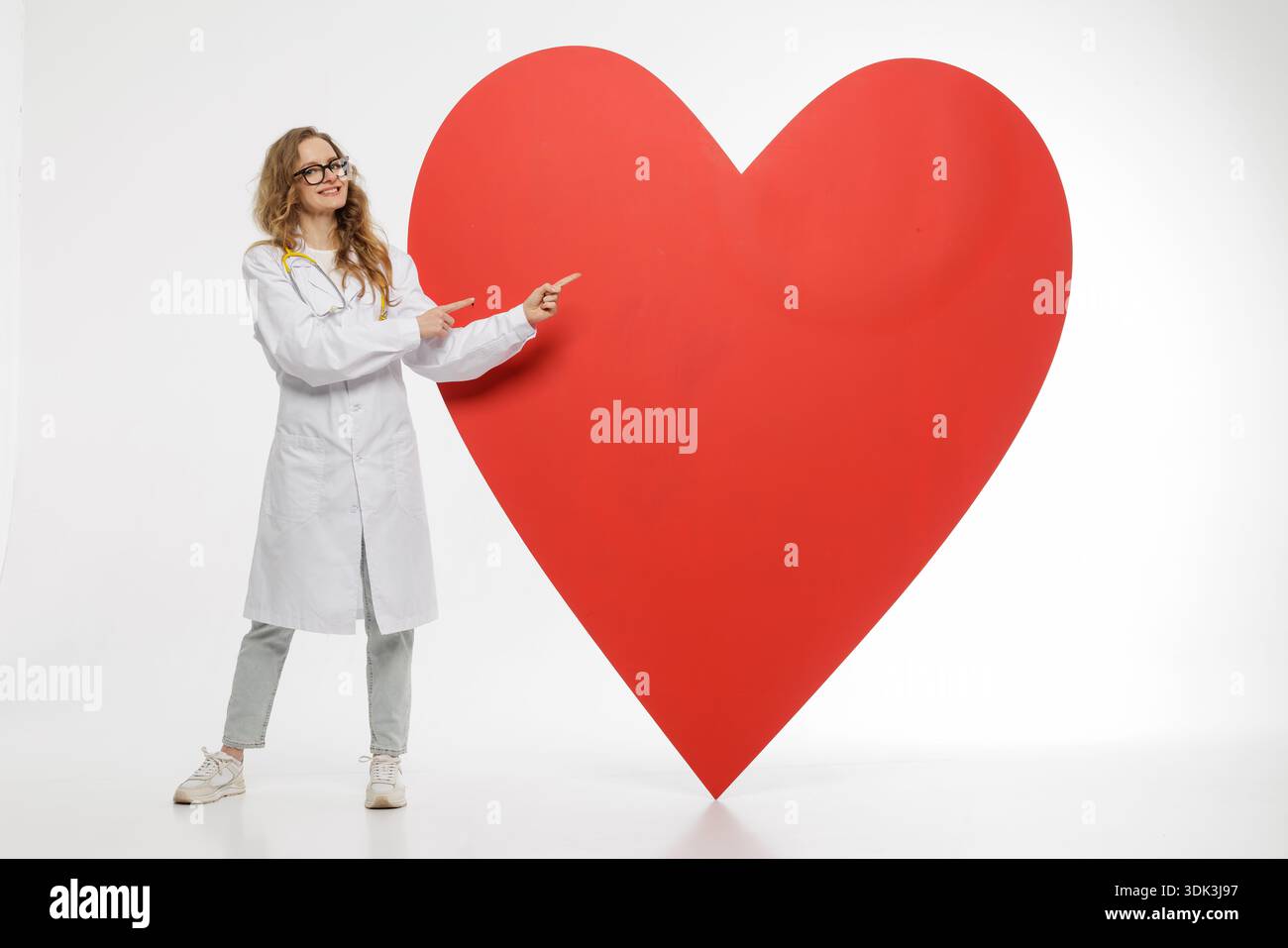 Medico donna in camice bianco punta su un grande simbolo rosso del cuore in studio. Immagine concettuale con spazio di copia per siti web pubblicitari e premiati nel settore sanitario Foto Stock