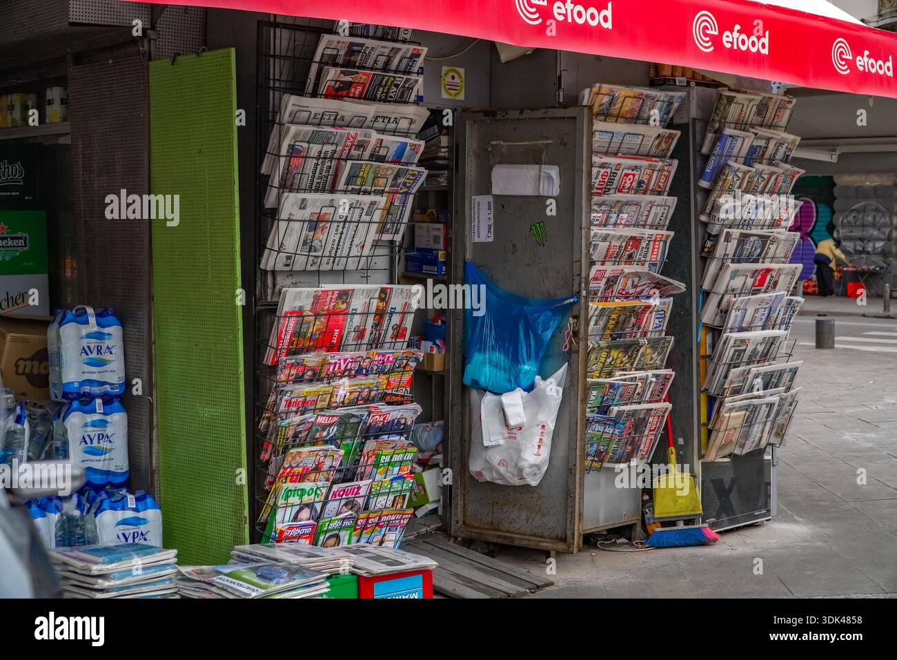 Chiosco greco di strada (Periptero) che vende giornali e riviste. Edicola urbana con stampa e acqua AVRA, Atene. Foto Stock