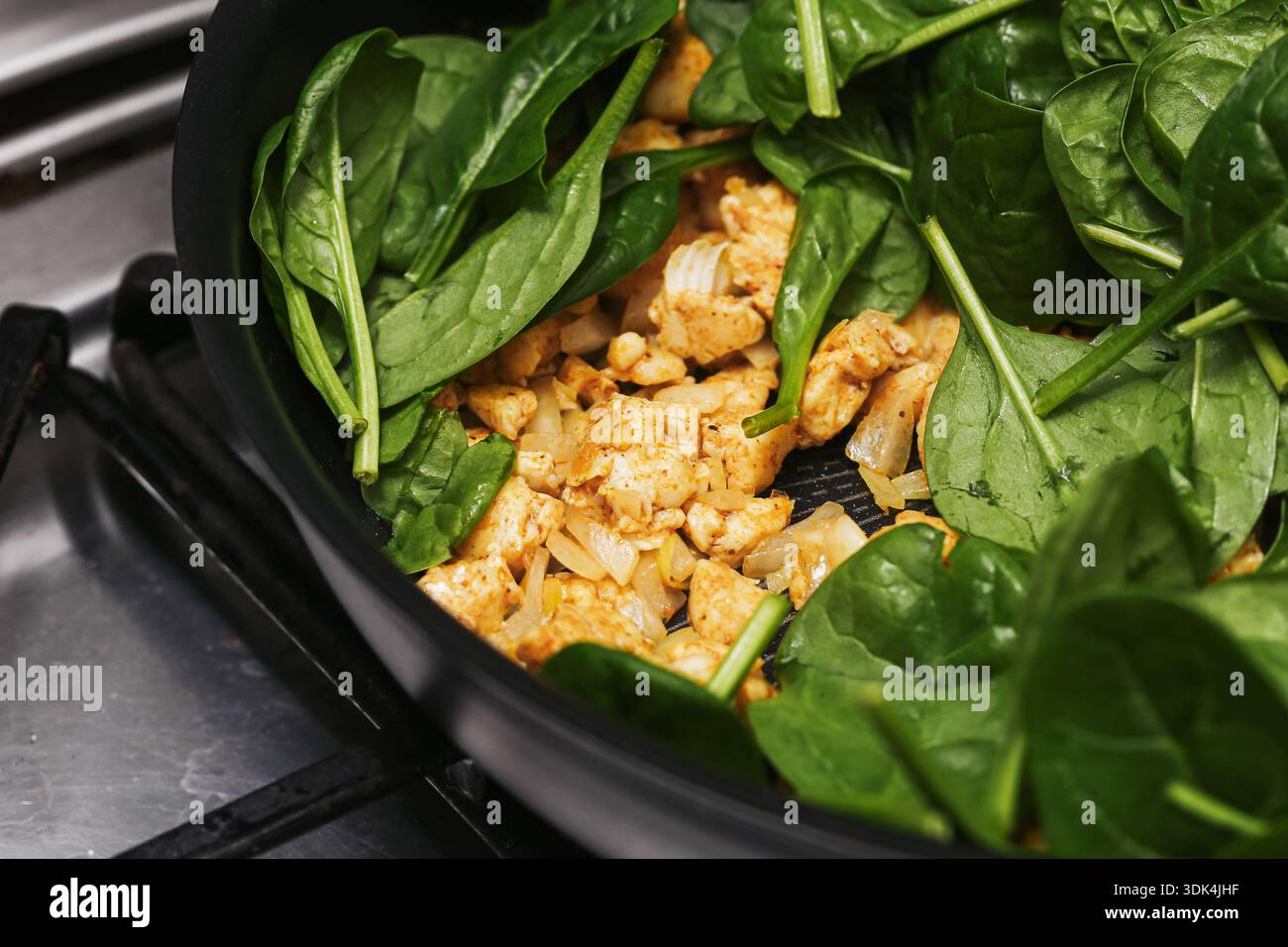 TITOLO: Cottura di spinaci e pollo in padella per friggere. Sana preparazione di pasti fatti in casa su piano cottura. Verdure verdi fresche con carne. Foto Stock