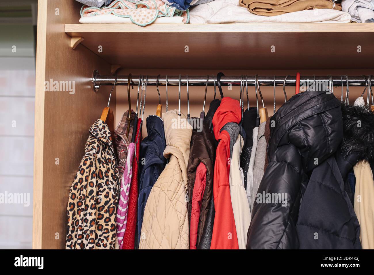 Guardaroba aperto con abiti appesi e giacche all'interno degli interni di casa. Deposito organizzato per abbigliamento stagionale e capispalla. Foto Stock