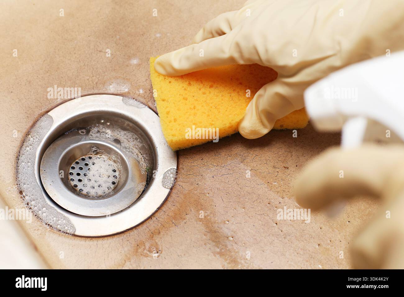 Pulizia dello scarico del lavandino della cucina con spugna e detergente spray. Rimozione di sporcizia e residui dall'area di scarico in metallo. Attività di igiene domestica. Foto Stock