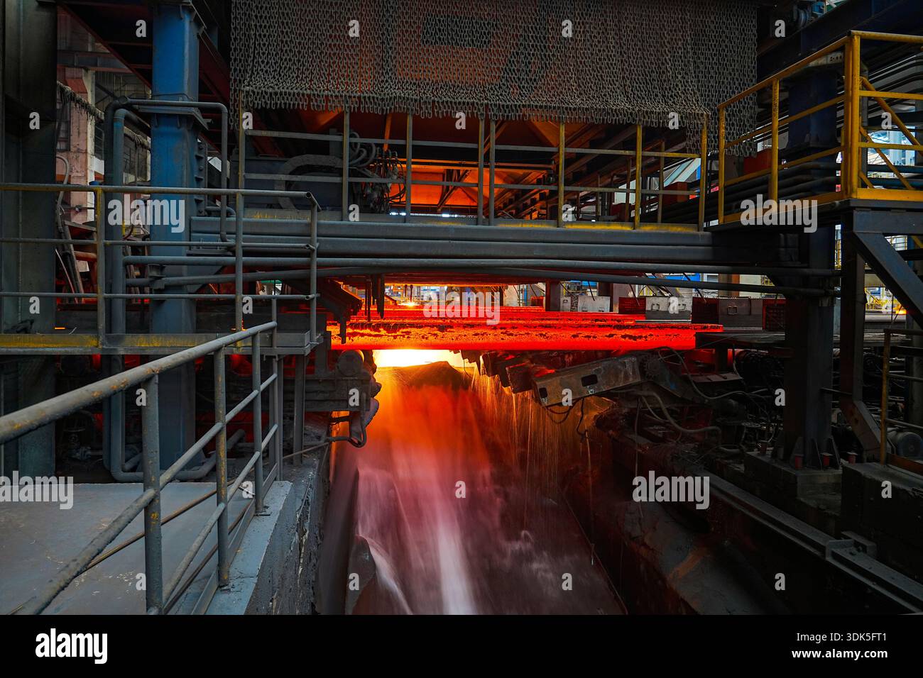 Nell'officina di laminazione a caldo di un'azienda siderurgica di medie dimensioni all'interno dell'impianto siderurgico, le billette di acciaio caldo rosso brillante vengono laminate attraverso il rotolo Foto Stock
