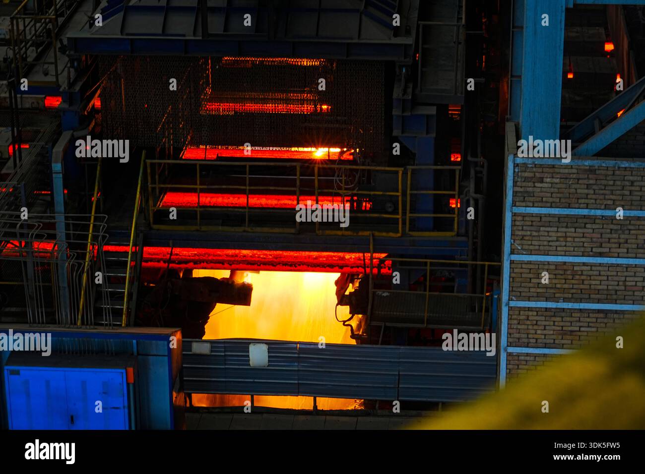 Nell'officina di laminazione a caldo di un'azienda siderurgica di medie dimensioni all'interno dell'impianto siderurgico, le billette di acciaio caldo rosso brillante vengono laminate attraverso il rotolo Foto Stock