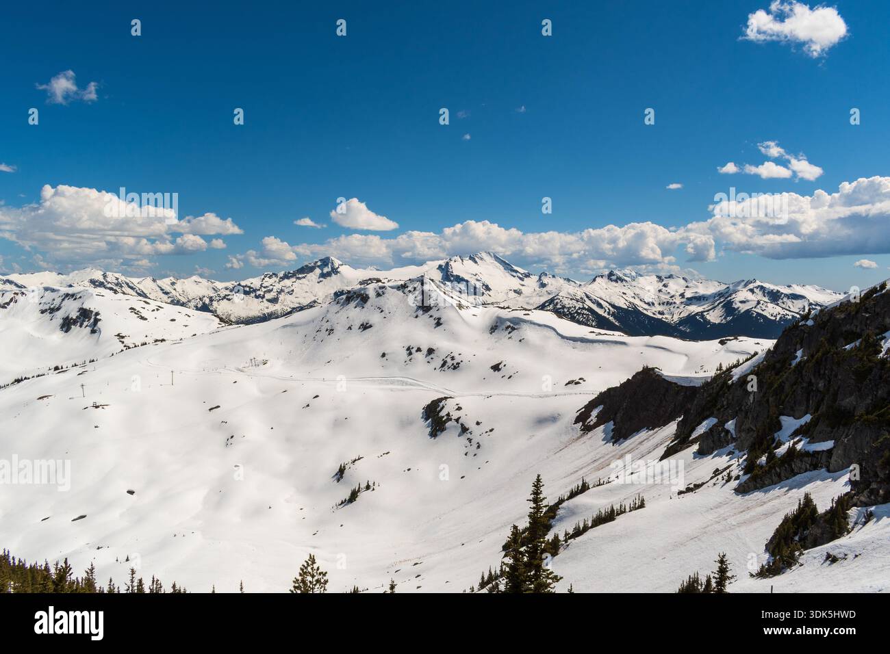 Una vista montana primaverile dal monte Whistler mostra picchi aspri, neve dissetante e un cielo luminoso con nuvole alla deriva. Foto Stock