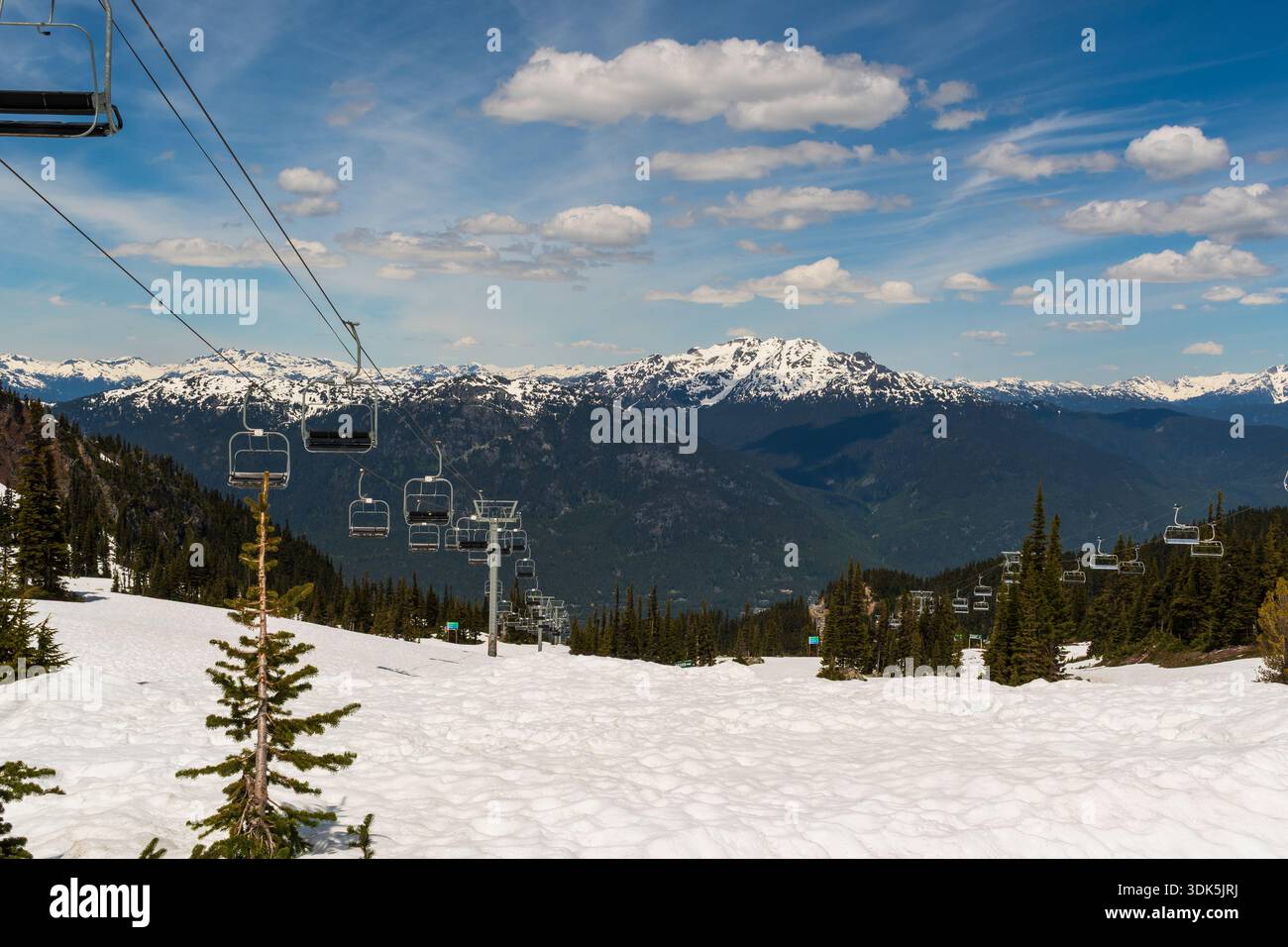 Whistler, BC Canada - 21 giugno 2024: Terreno innevato e vette di montagna lontane con impianti di risalita sotto un cielo blu. Foto Stock