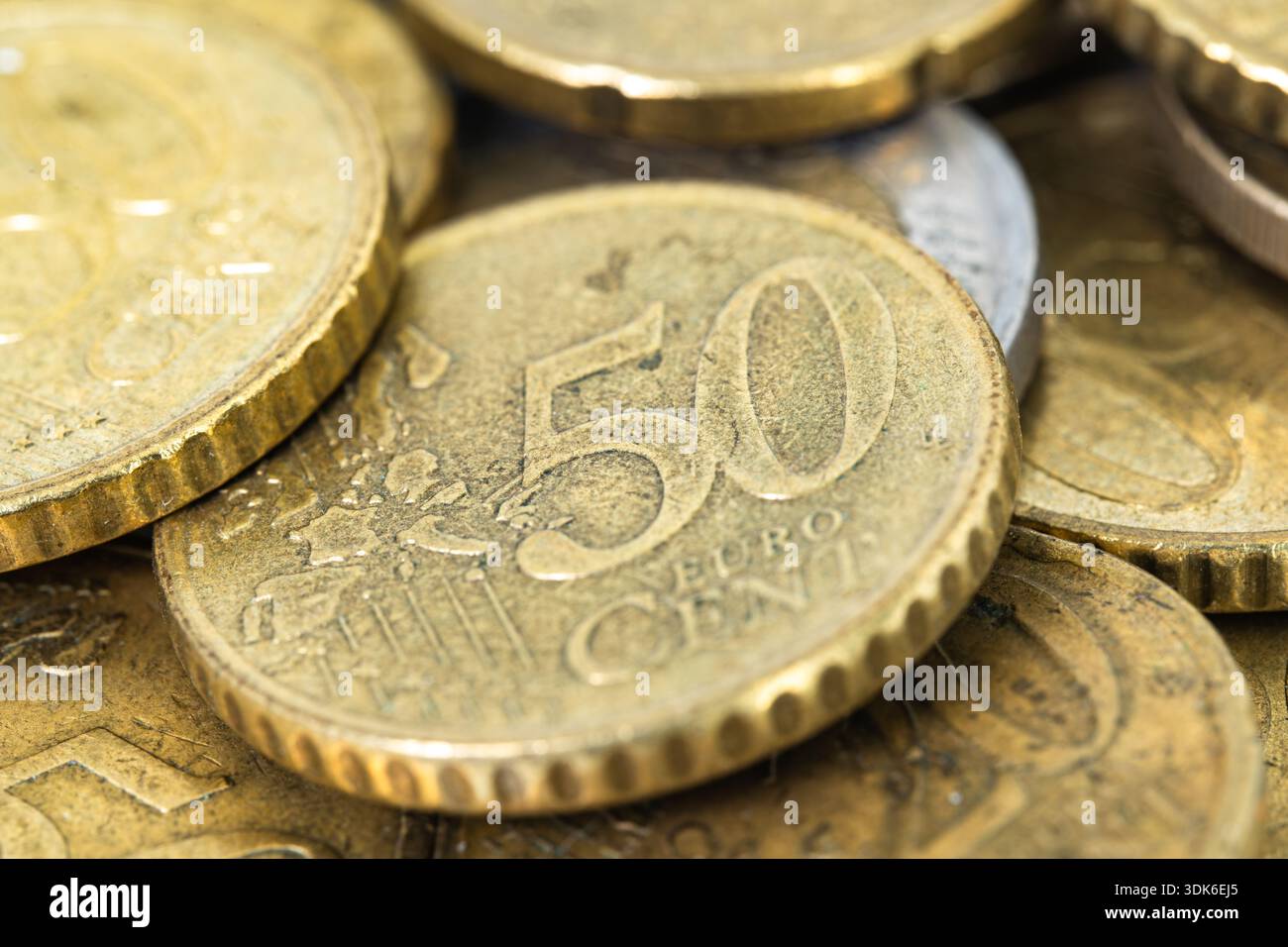 La scena mostra un mix di monete in euro disposte su una superficie. Sono visibili diversi tagli, concentrandosi sulla moneta da 50 centesimi. Le monete riflettono la luce Foto Stock