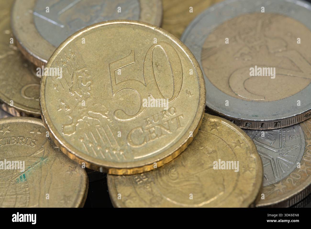 La scena mostra un mix di monete in euro disposte su una superficie. Sono visibili diversi tagli, concentrandosi sulla moneta da 50 centesimi. Le monete riflettono la luce Foto Stock