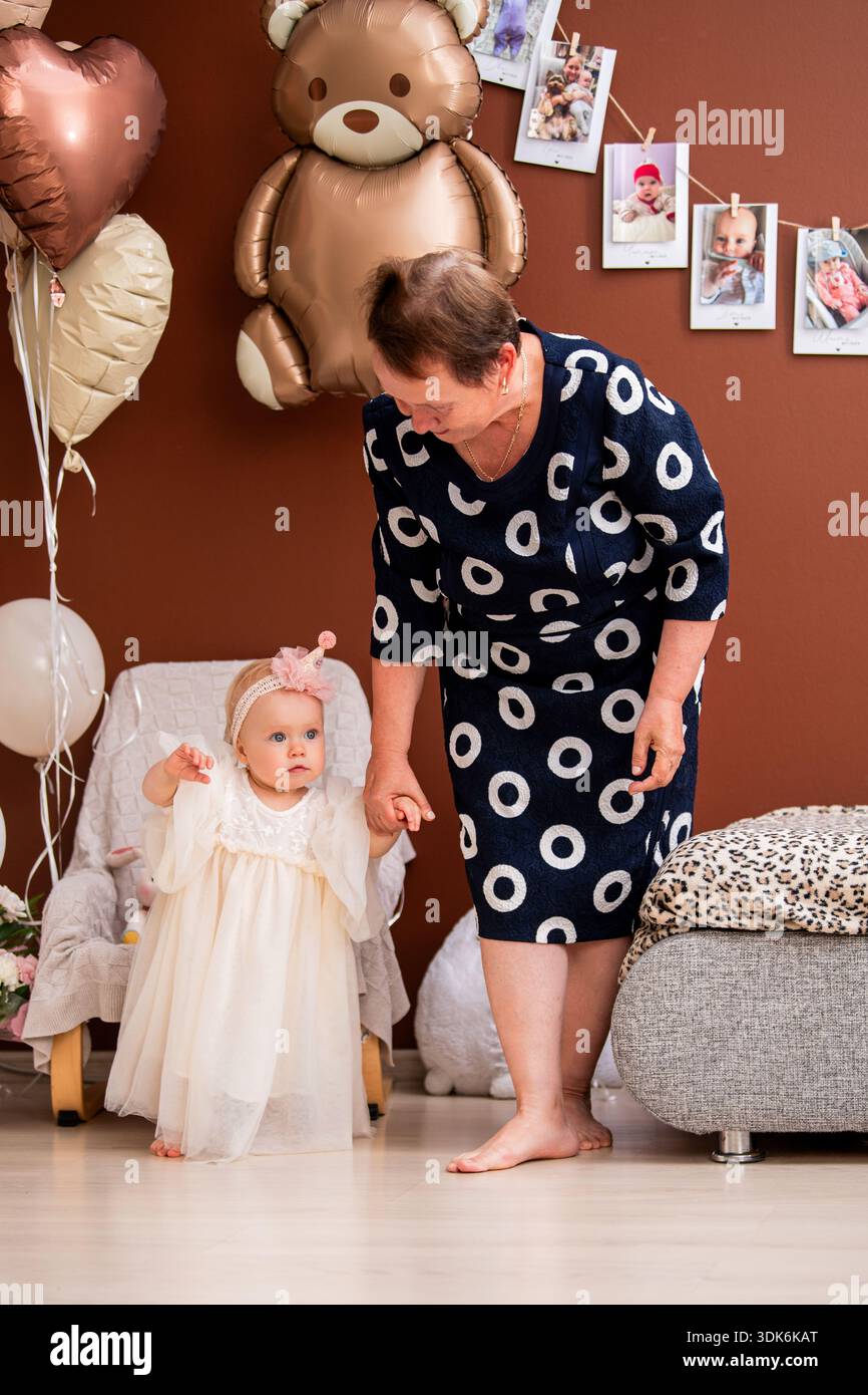 La nonna aiuta la bambina a fare i primi passi durante il primo compleanno Foto Stock
