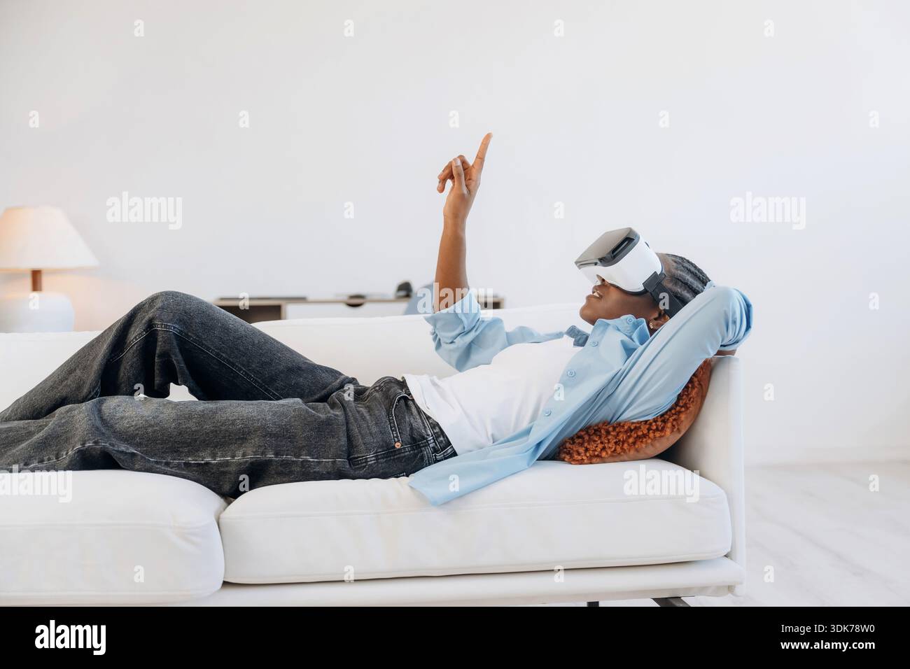 Vista laterale, sdraiato e indossato il visore VR. La donna è a casa in una stanza domestica. Foto Stock