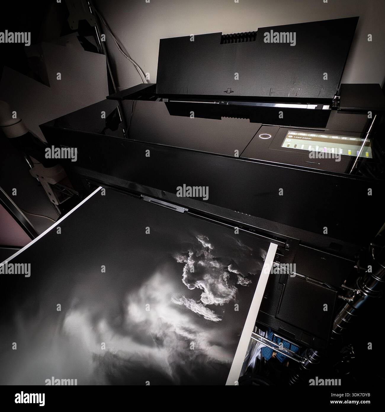 La stampante per grandi formati Epson espelle una stampa orizzontale in bianco e nero in una configurazione studio con illuminazione da tavolo Foto Stock