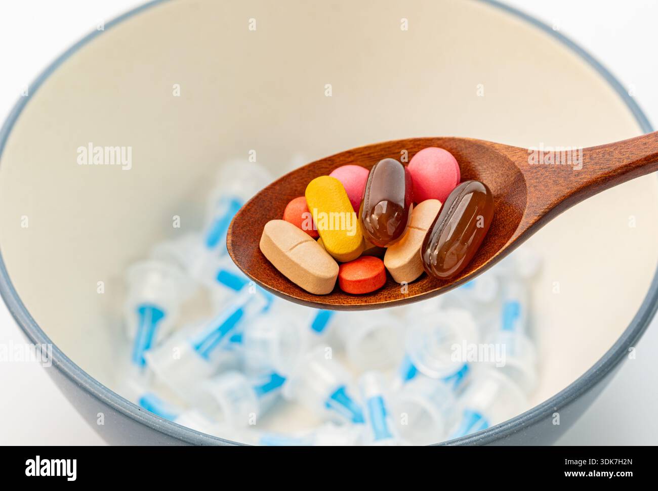 Concetto di scelta medica tra farmaci orali e iniezioni. Cucchiaio di legno pieno di pillole colorate e integratori su uno sfondo di molti utilizzati Foto Stock