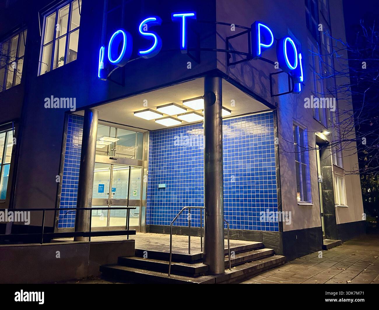 Vista esterna di un ufficio postale di notte con un cartello blu al neon che illumina la strada buia. - Immagine stock catturata con smartphone