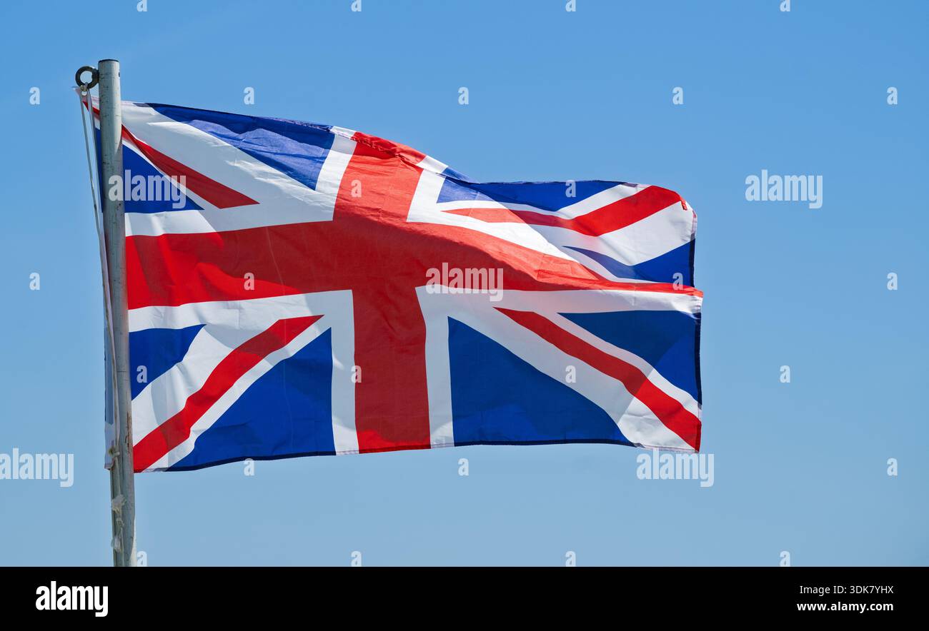 Bandiera Union Jack che soffia nel vento contro un cielo azzurro. Lancashire, Regno Unito. Foto Stock