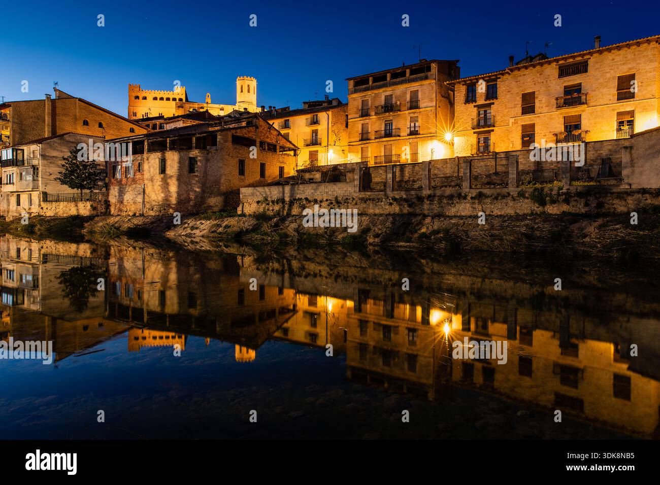 Città notturna sul fiume con luci calde e Ponte di pietra ad arco che si riflette in acque calme, Valderrobres, Spagna Foto Stock