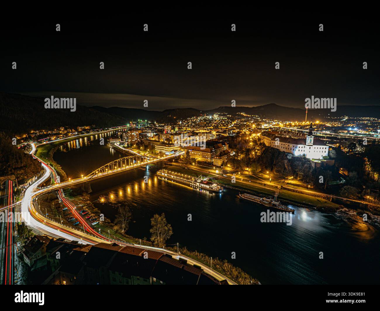 Paesaggio urbano notturno con ponti illuminati, riflessi fluviali e percorsi luminosi a lunga esposizione della città di Děčín. Foto Stock