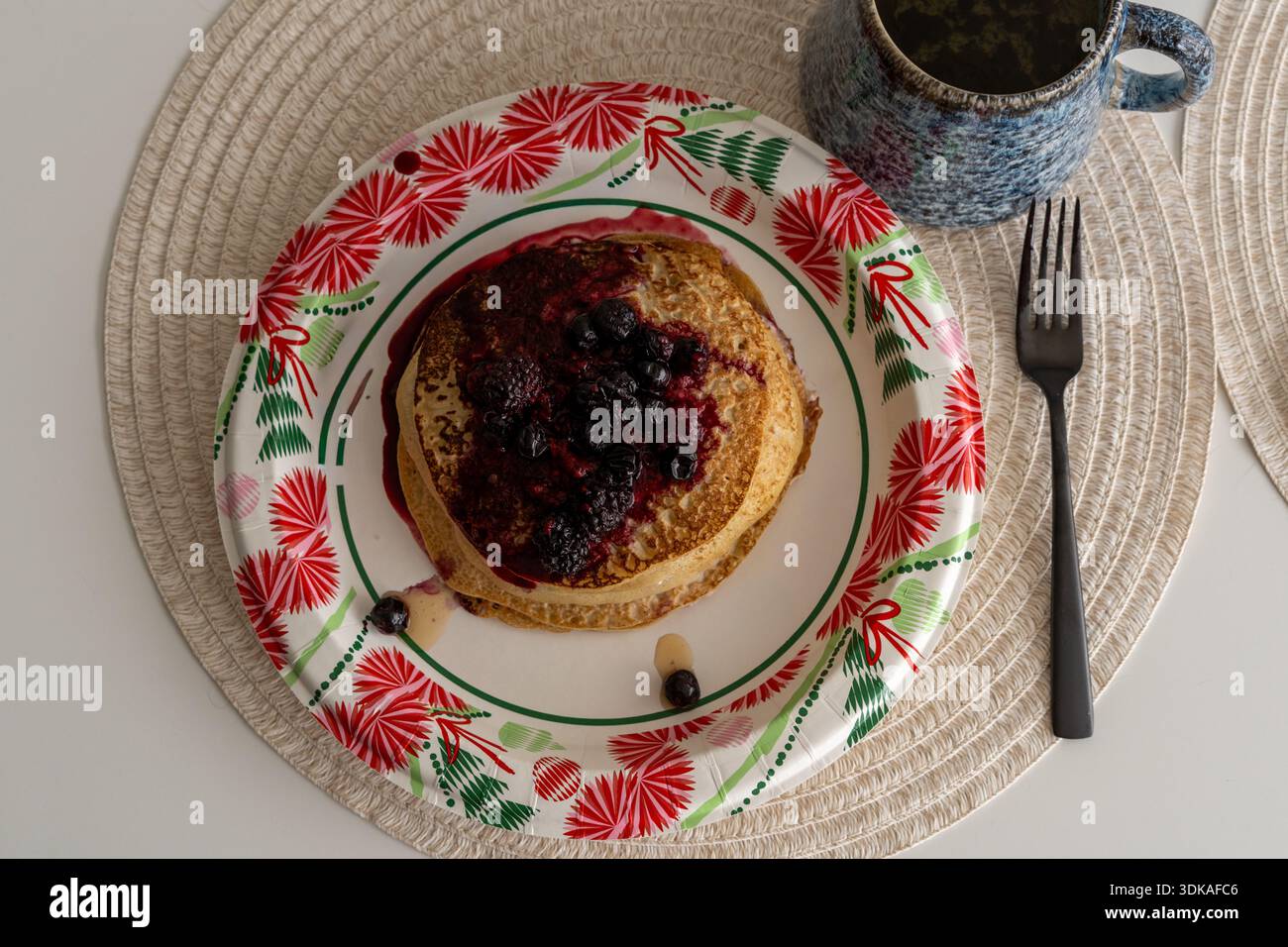 Colpo sopra la testa di una deliziosa pila di soffici pancake ricoperti di frutti di bosco freschi, conditi con sciroppo e serviti su un piatto di carta. Un perfetto, semplice Foto Stock