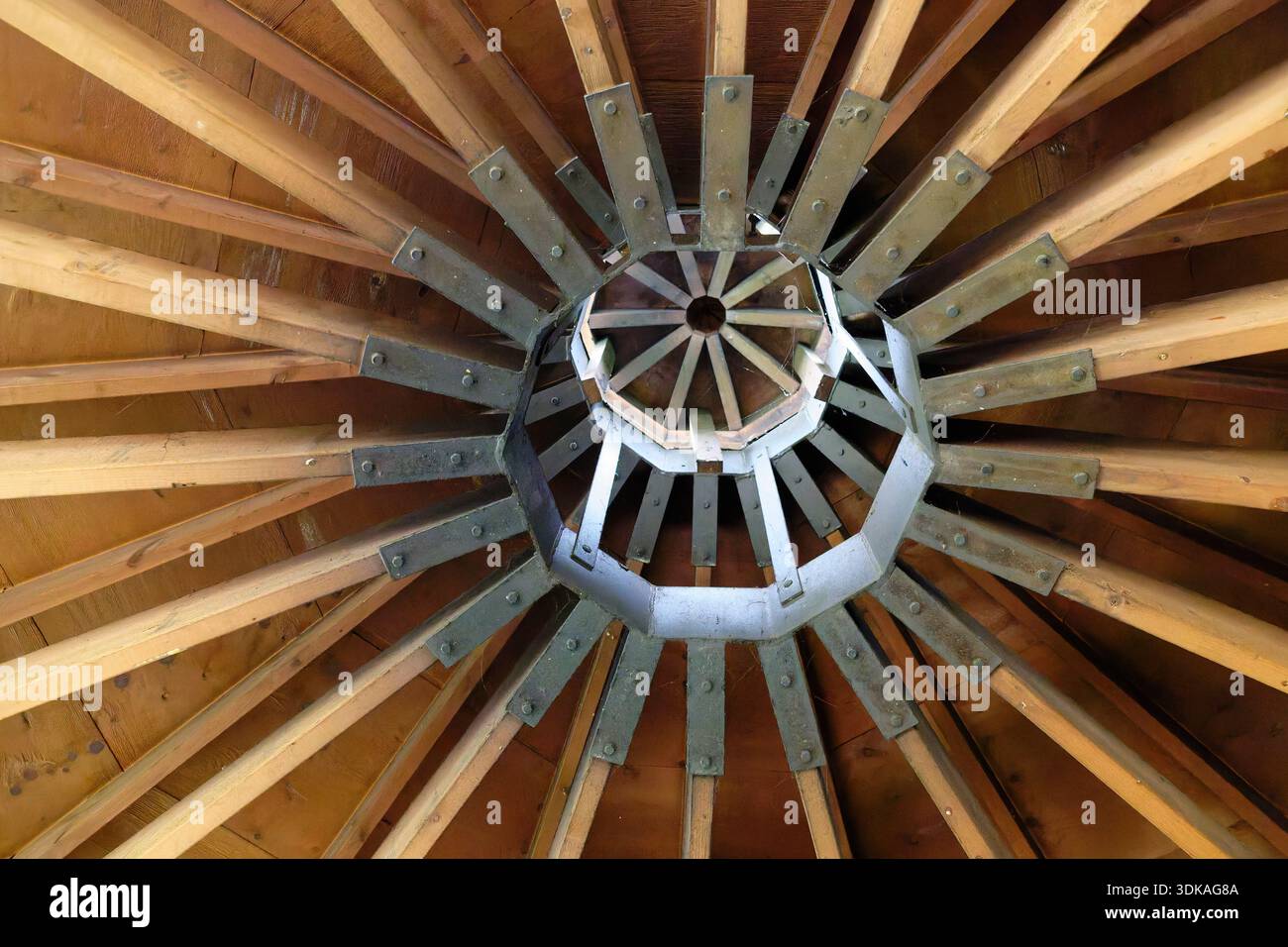 Le travi del tetto si innalzano verso l'interno fino a raggiungere un mozzo metallico sotto un tappo, lasciando uno spazio di ventilazione protetto che consente all'aria di circolare naturalmente attraverso il gazebo in legno Foto Stock