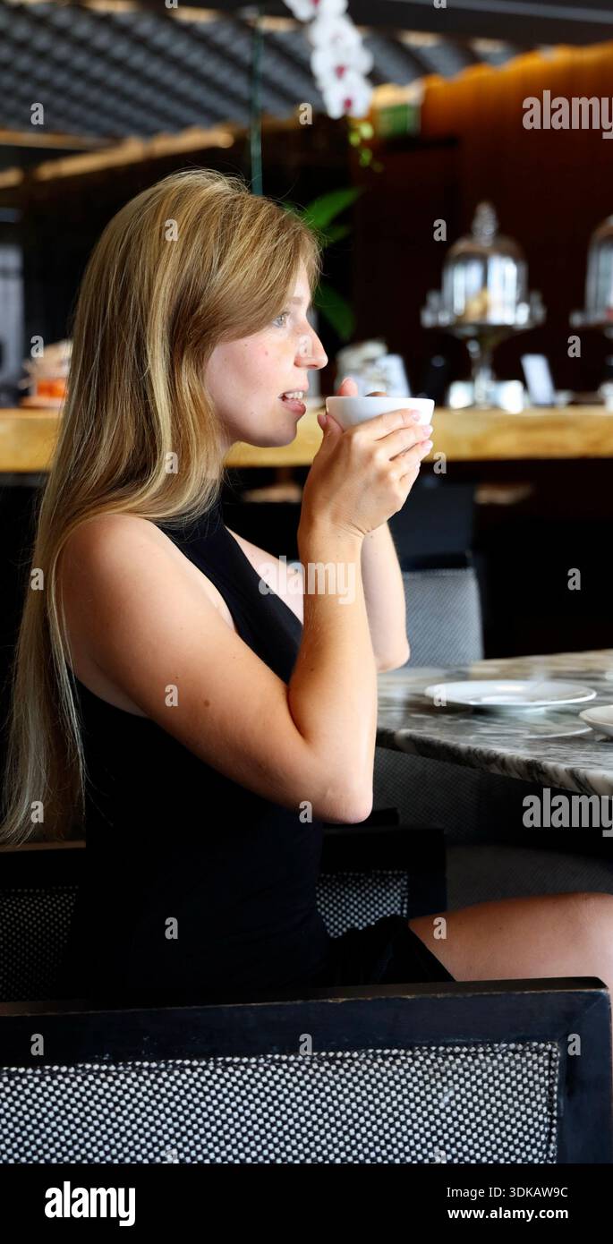 Giovane donna sofisticata che gusta una bevanda mattutina in un ristorante di lusso. Stile di vita elegante e concetto di ospitalità per il marchio di lusso Foto Stock