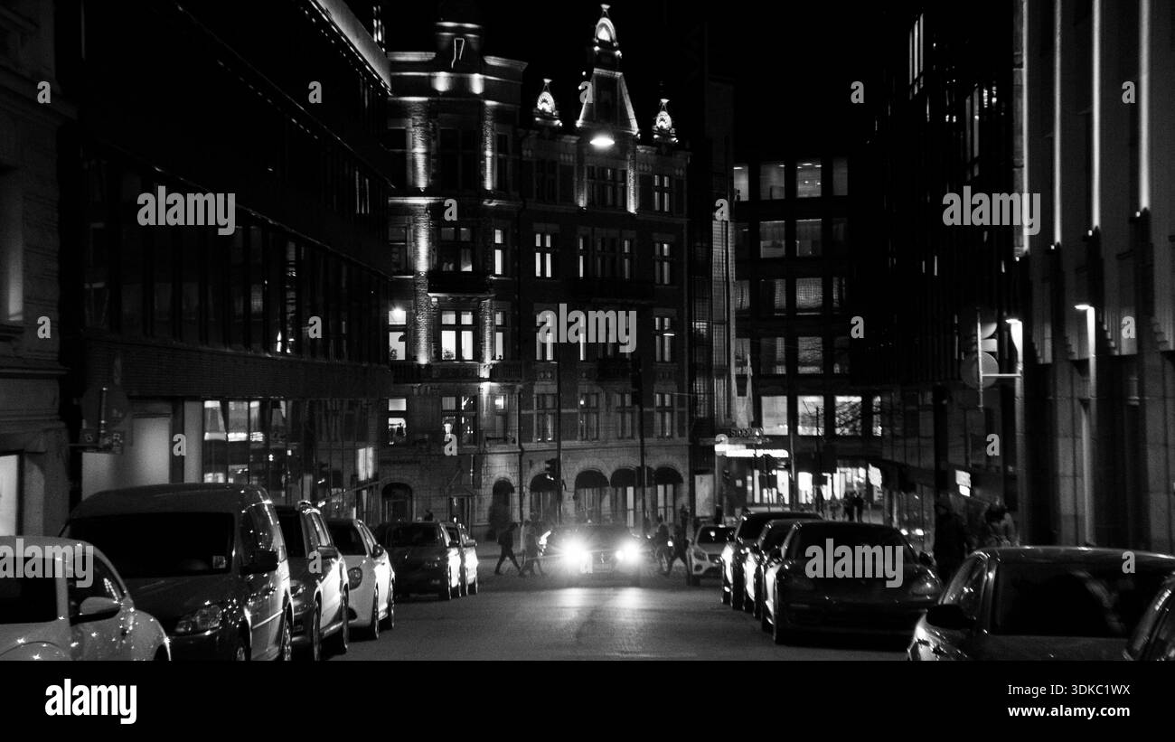 Strada bianca e nera di notte con architettura storica illuminata e auto parcheggiate, che rappresenta la vita urbana, i viaggi e la moderna città europea Foto Stock