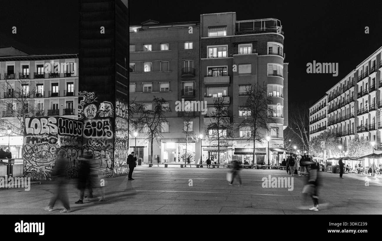 Scena notturna a Madrid mentre figure sfocate attraversano una piazza della città vicino a un museo importante, catturando il movimento urbano e la vita di strada contemporanea. Foto Stock