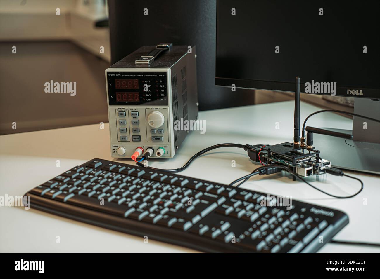 Area di lavoro per l'ingegneria elettronica con alimentatore da banco, tastiera per computer, monitor e una piccola scheda a circuito stampato wireless con antenna Foto Stock