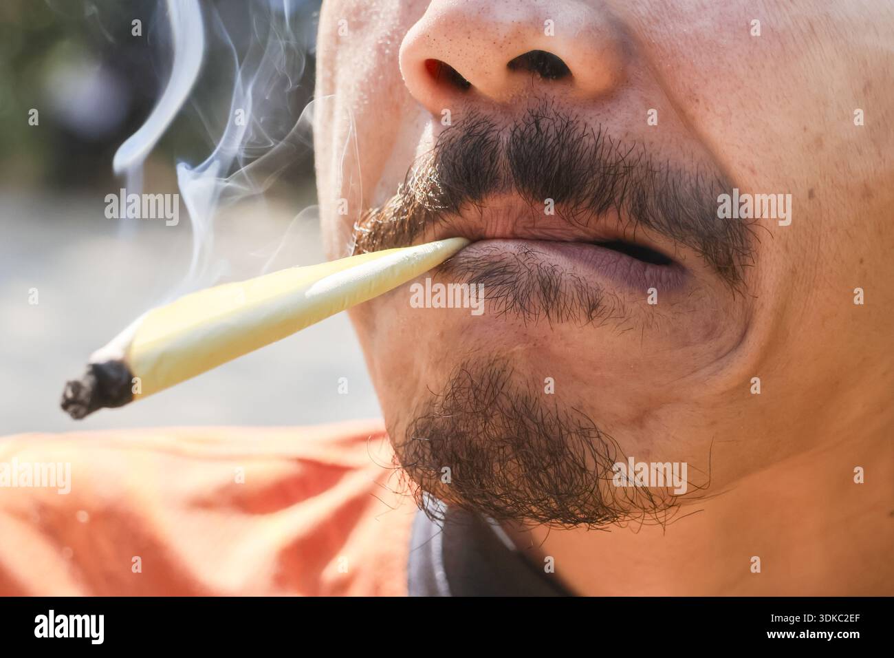 Primo piano di un uomo rilassato che fuma marijuana. Fumo bianco proveniente dalla bocca di una persona che usa cannabis per scopi ricreativi o medici Foto Stock