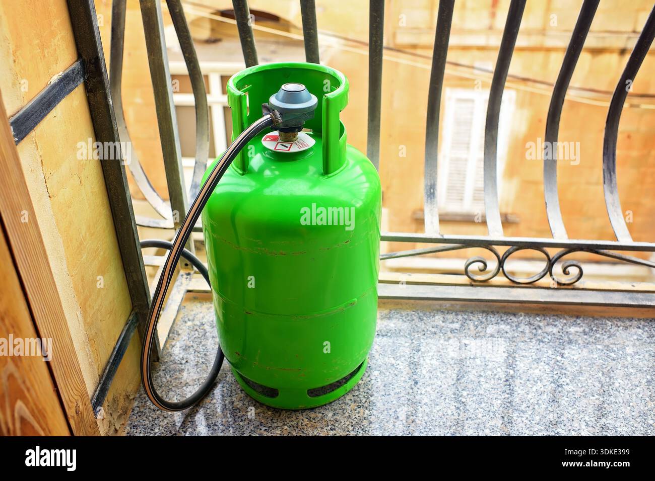 Vista di una bombola GPL verde con regolatore di pressione e tubo flessibile su un balcone utilizzato per cucinare in appartamenti nei paesi mediterranei. Foto Stock