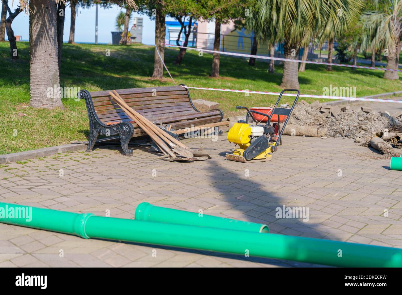 Area di costruzione in parco con tubi, banco, compattatore e nastro di avvertenza Foto Stock