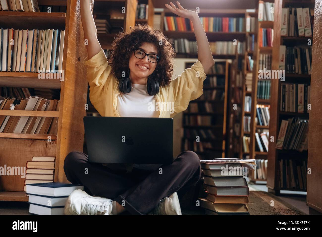 Con le cuffie e con il computer portatile, seduto. Una bella donna è in biblioteca. Foto Stock