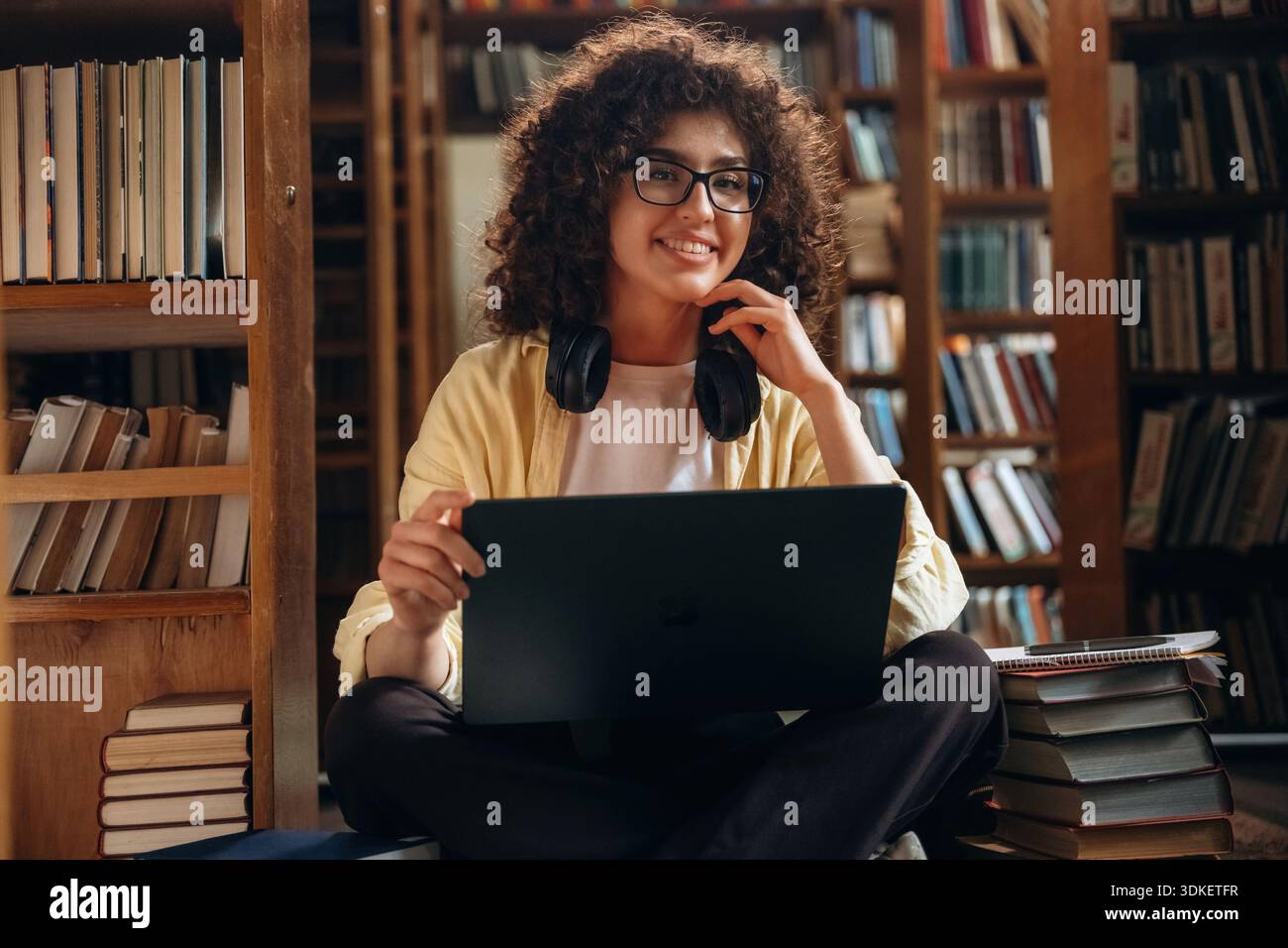 Con le cuffie e con il computer portatile, seduto. Una bella donna è in biblioteca. Foto Stock