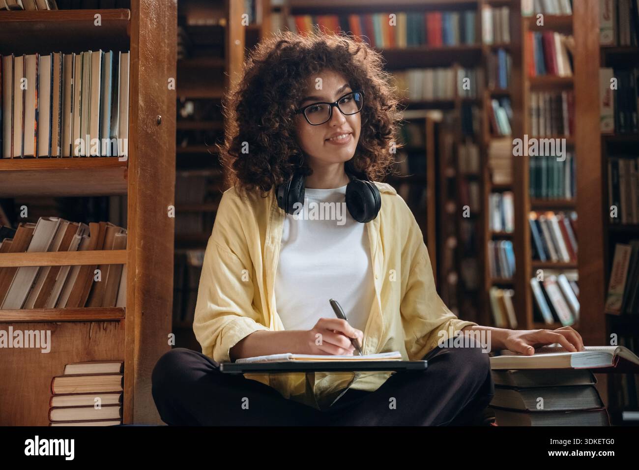 Il processo di scrittura. Con penna e cuffie. Una bella donna è in biblioteca. Foto Stock