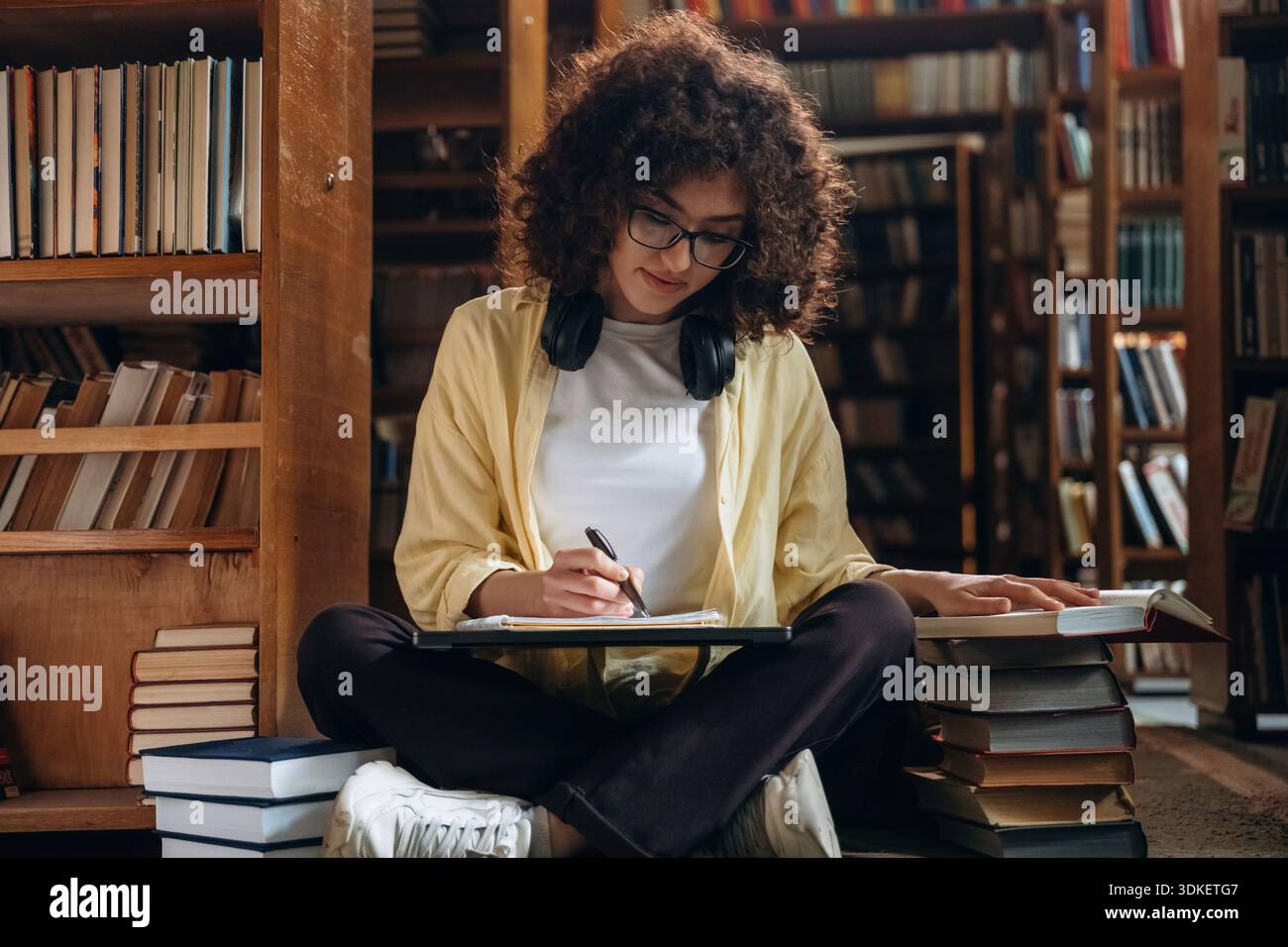 Il processo di scrittura. Con penna e cuffie. Una bella donna è in biblioteca. Foto Stock