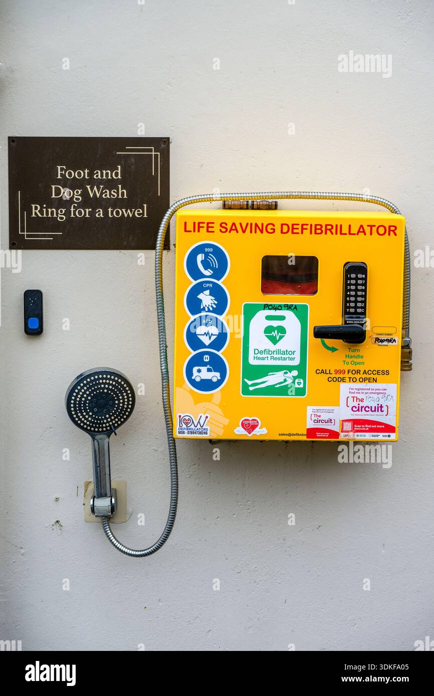 Defibrillatore pubblico e lavaggio di piedi e cani sulla parete di un hotel con un cartello che chiede agli utenti di suonare per un asciugamano. Foto Stock