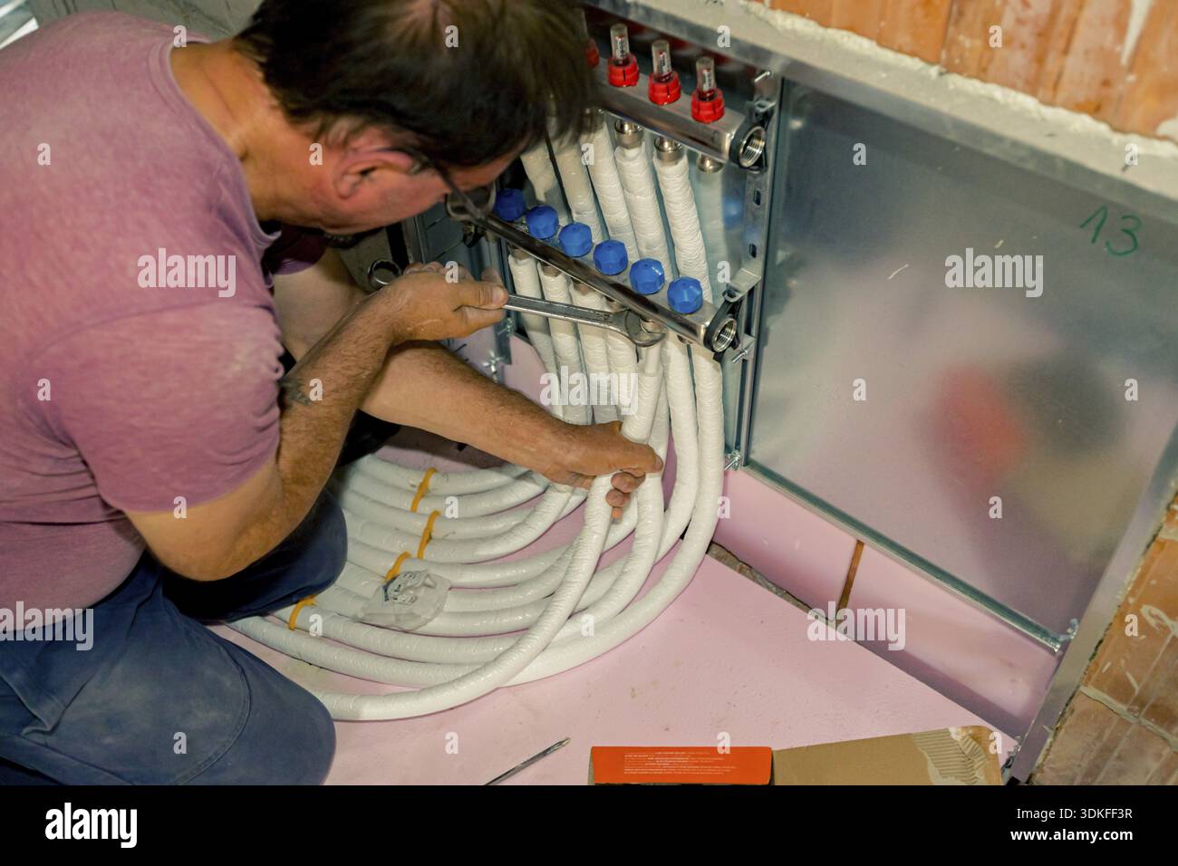 Montaggio dei lavoratori nuove valvole collettore del sistema di distribuzione in ottone montate per il riscaldamento centralizzato del pavimento in un edificio residenziale in costruzione Foto Stock
